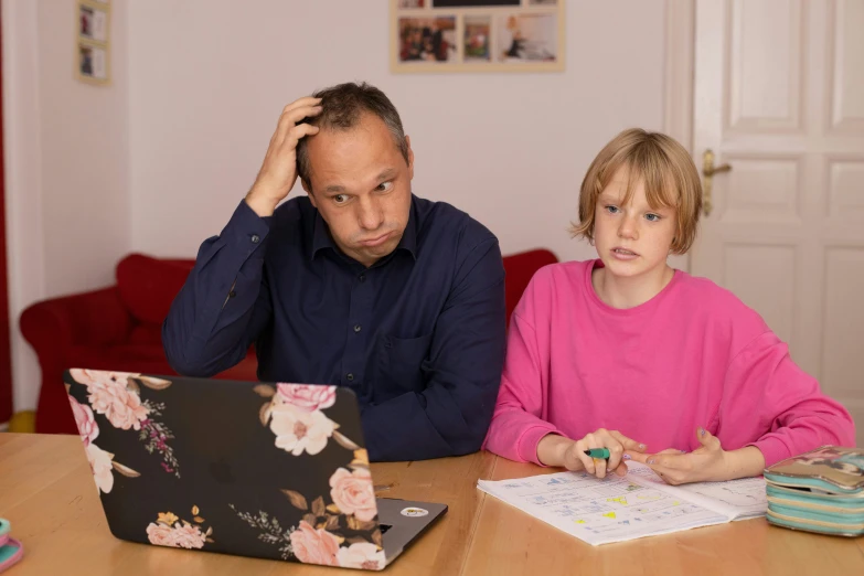 a man is looking at his laptop while his daughter sits at her desk