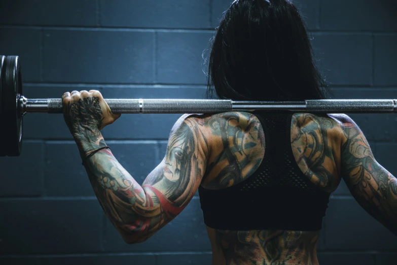 a tattooed woman lifting a barbell in the gym