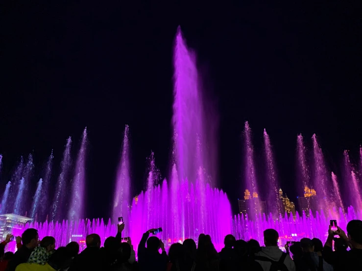 people are gathered around brightly colored fountains in the night sky