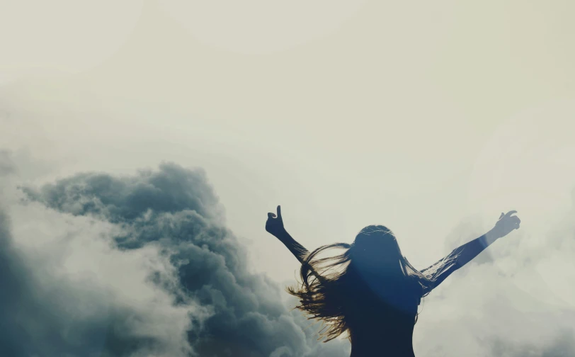 silhouette of a woman with hands up in front of a cloudy sky