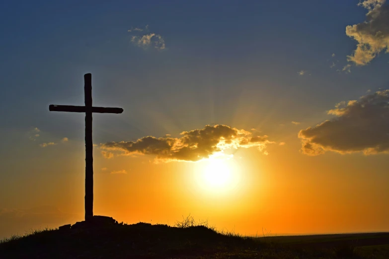 a cross in the middle of a hill near sunset