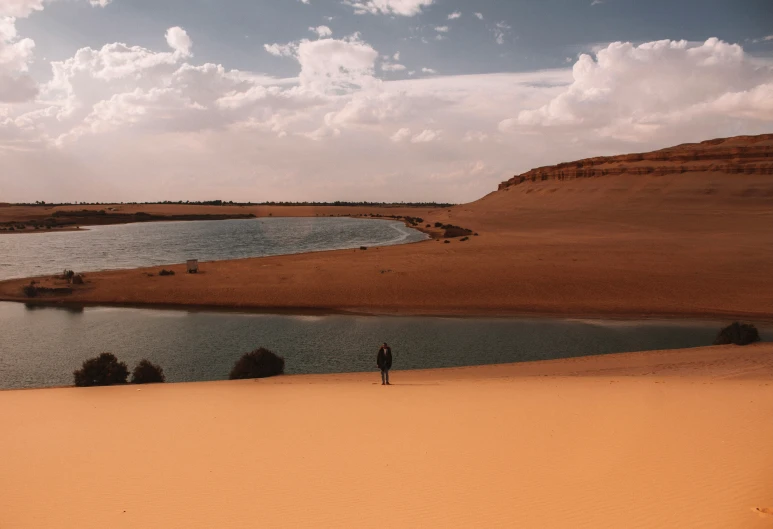 a lone person standing at the edge of a large river in the middle of a plain