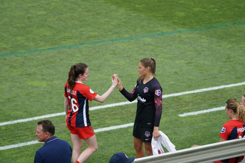 two female soccer players are high fiving on the sidelines