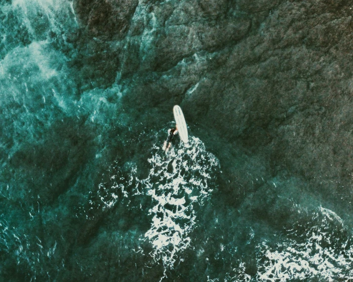 an aerial view of a surfer paddling their board