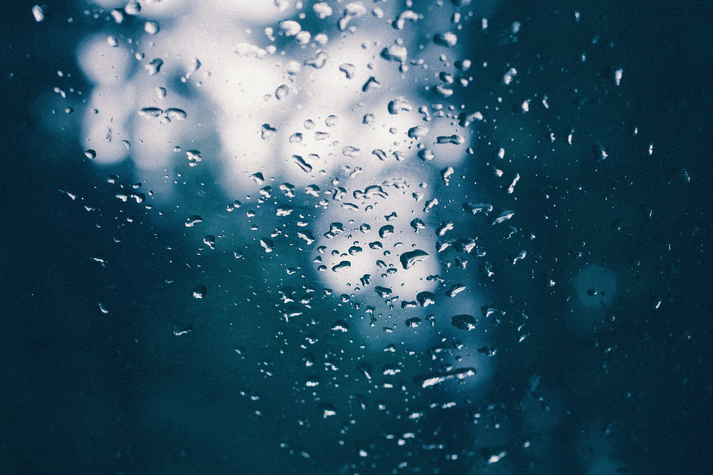 rain drops hanging from a glass with trees in the background