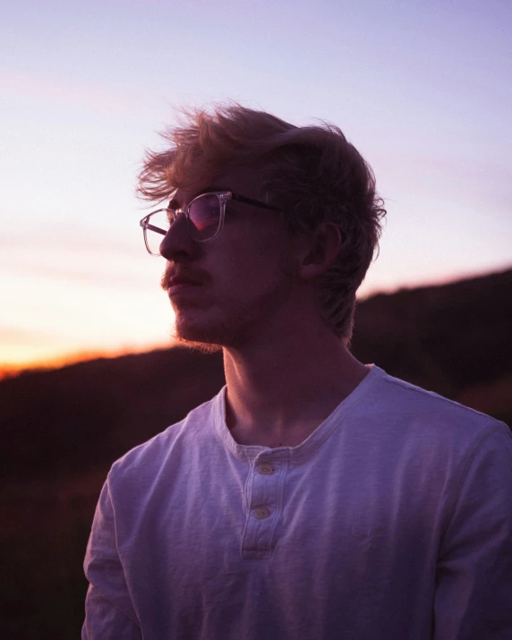 a man in glasses standing on a hill top