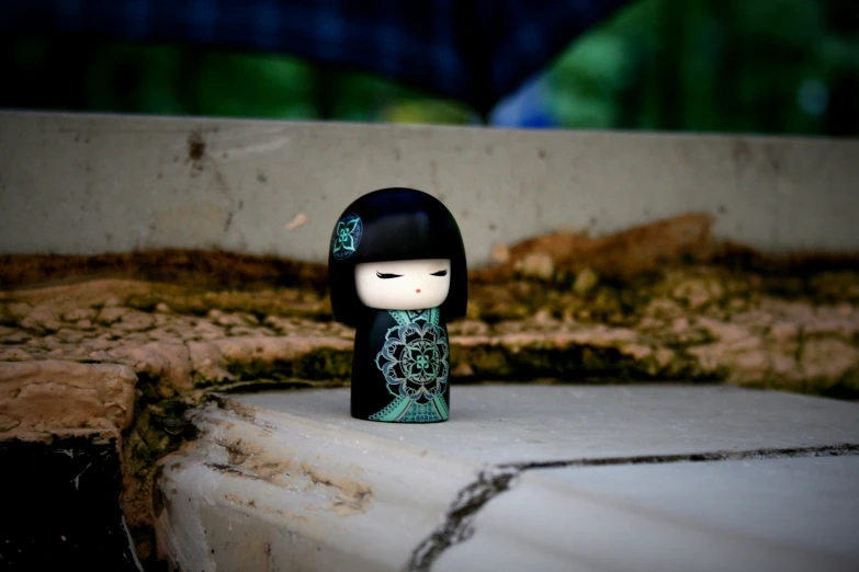 small doll sitting in front of a cement slab