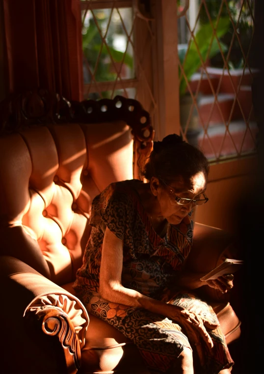 a woman sits on a chair next to a window reading