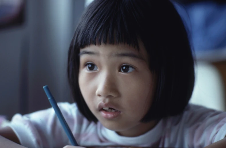 a little girl sitting at a table and looking into the camera