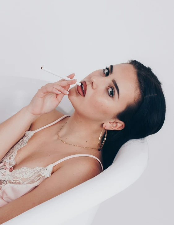 an asian woman in lingerie sitting in a tub with a cigarette