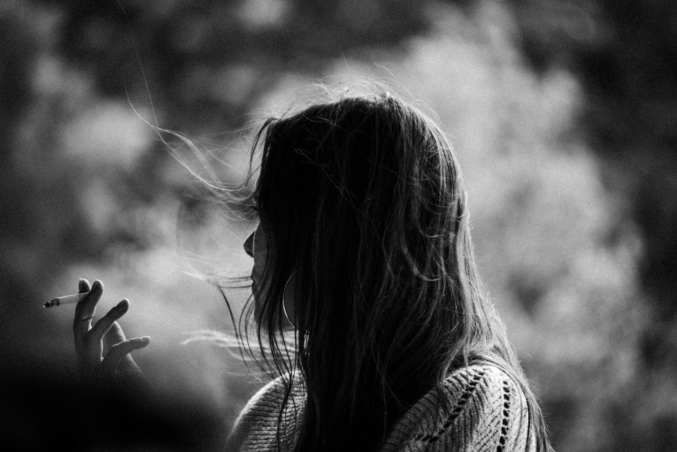 a dark haired woman smoking a cigarette with a foggy background