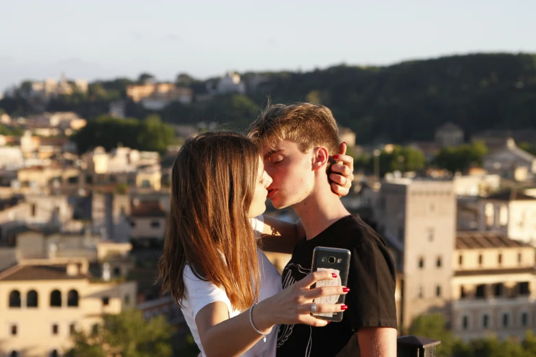 two young people share a kiss on a balcony overlooking the city