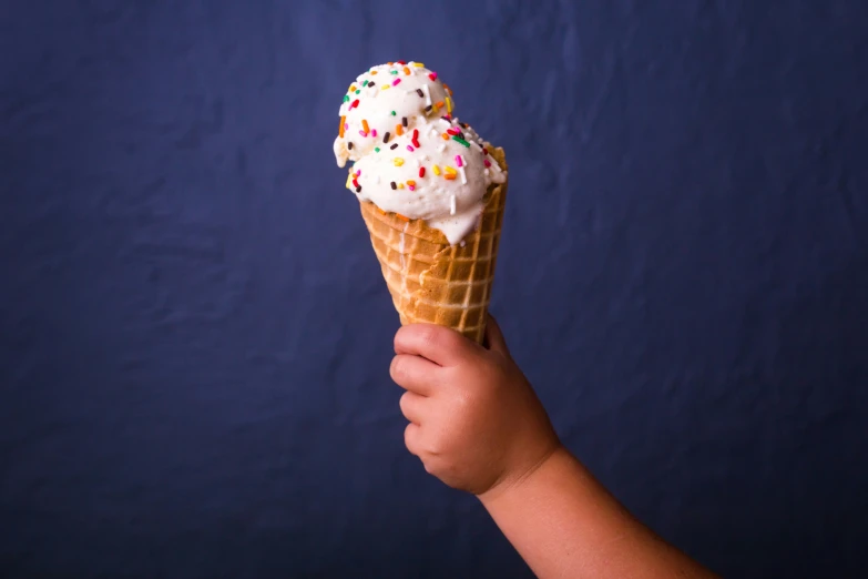 a hand holding an ice cream cone with sprinkles