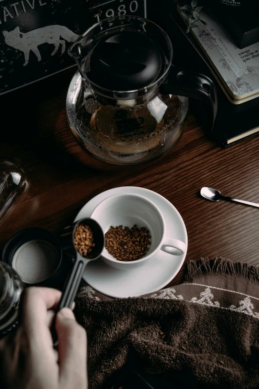 a person sitting at a table with a white bowl full of cereal and a glass tea pot