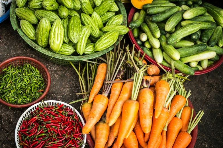 a bunch of assorted carrots in baskets next to other bowls of various vegetables