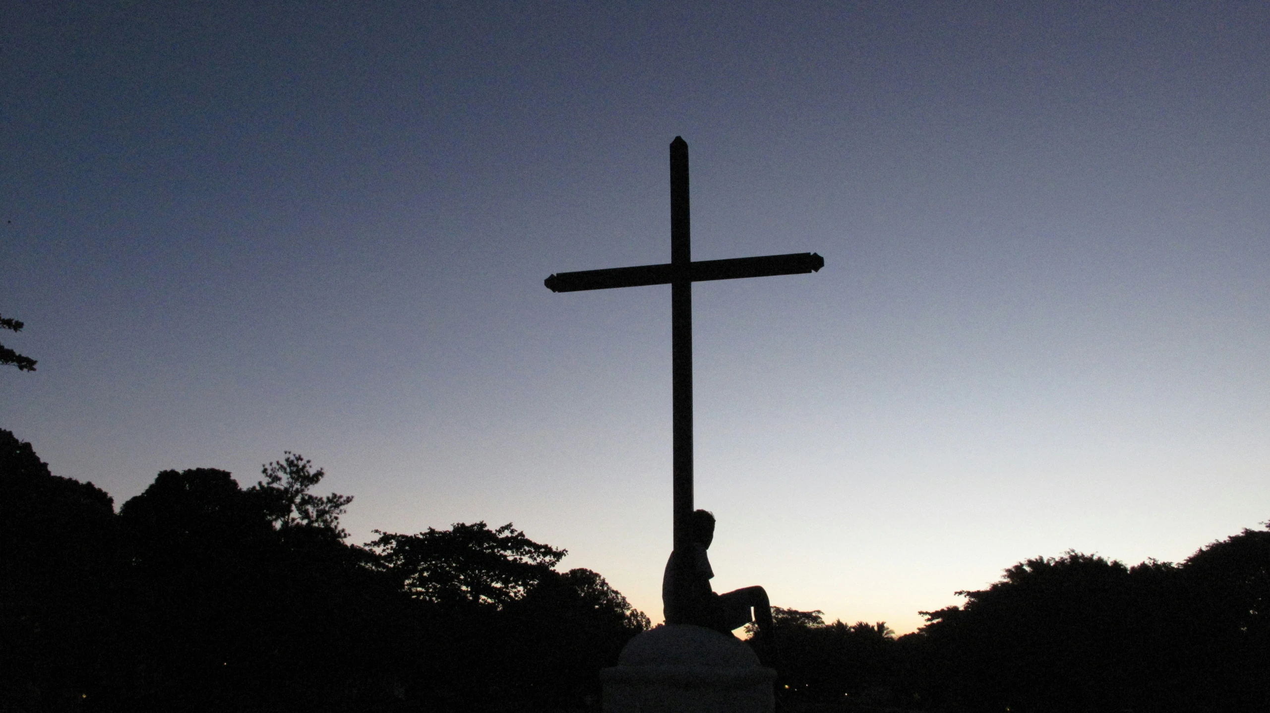 a cross sitting in the middle of a forest at dusk