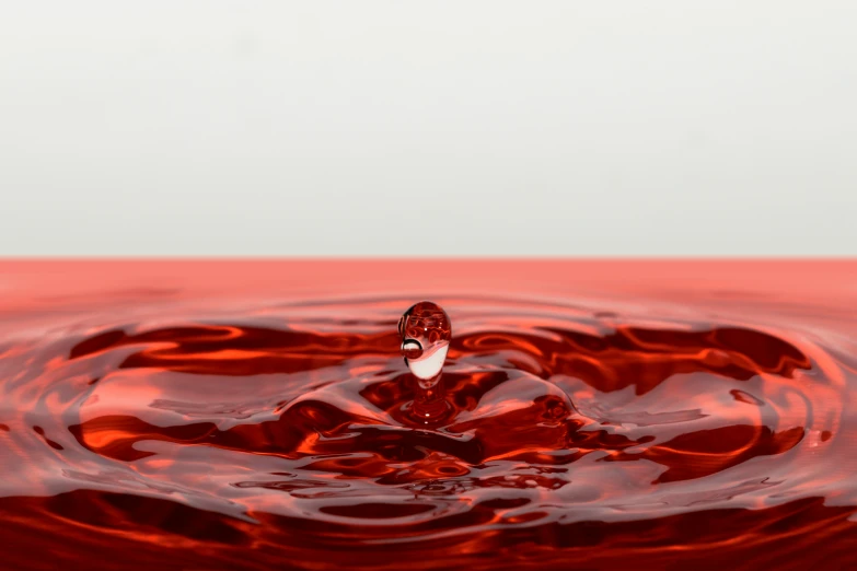 red liquid droplet with ripples in a large pool