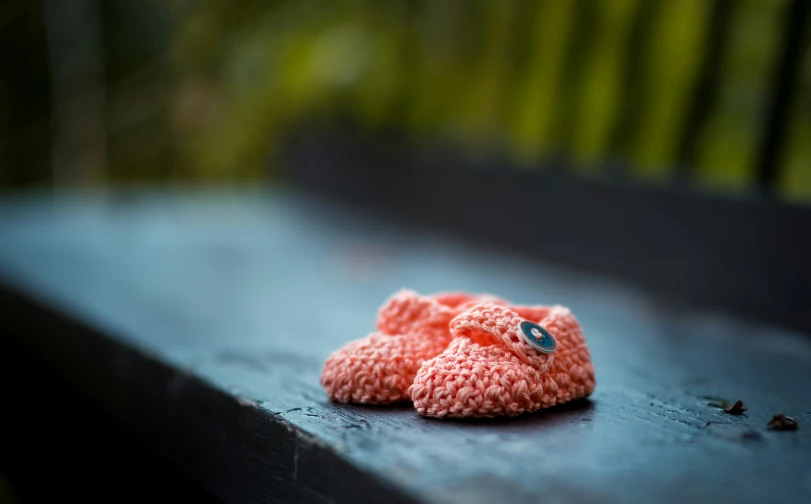 a knitted pink teddy bear on a wooden bench