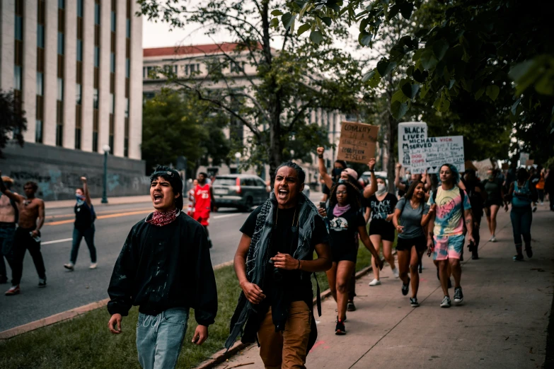 a group of people walking down a sidewalk with a woman carrying a sign in front of them