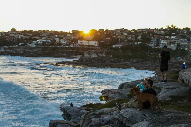 three people at the water's edge on a cliff overlooking some city