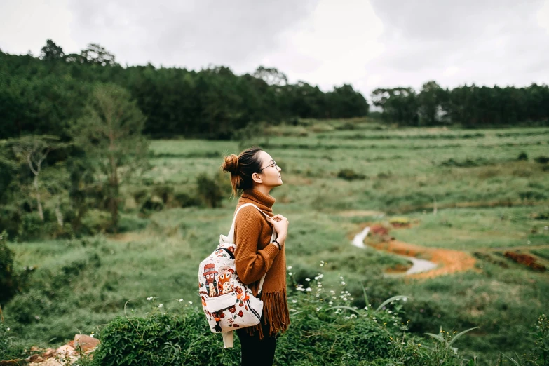 a woman standing on a grassy hillside next to a forest