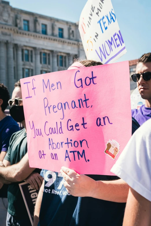 man in glasses is holding a pink sign and another man has another sign