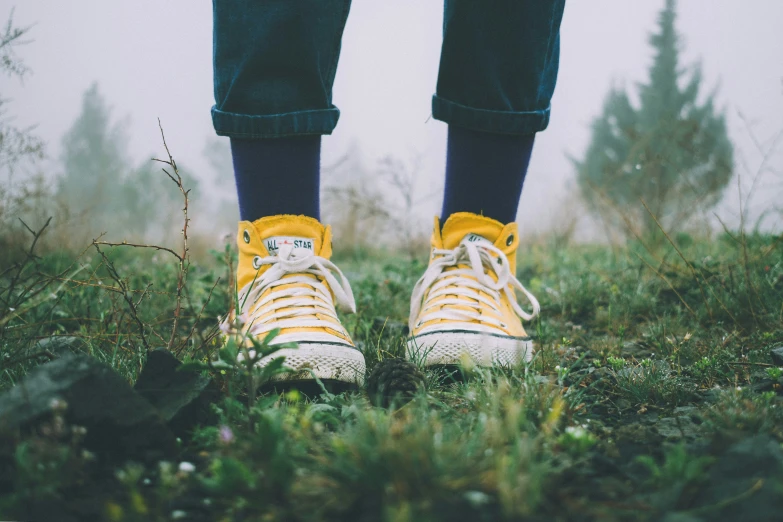 a person wearing yellow sneakers standing in grass