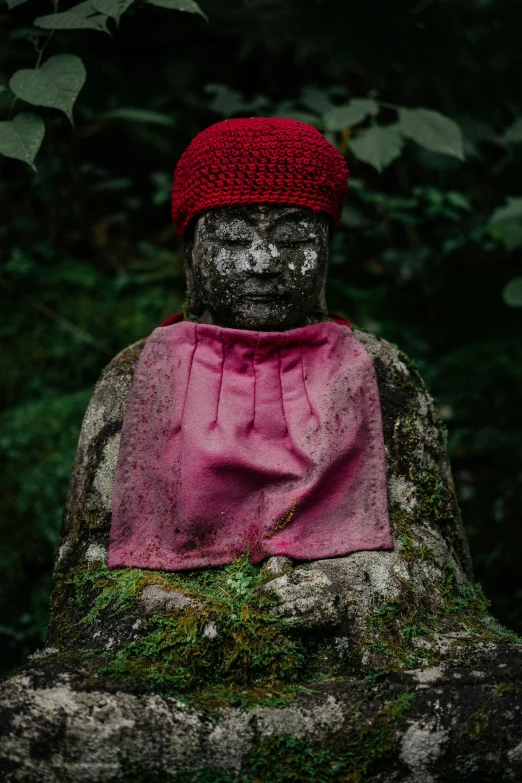 a stone statue covered in a red fabric sitting in the forest