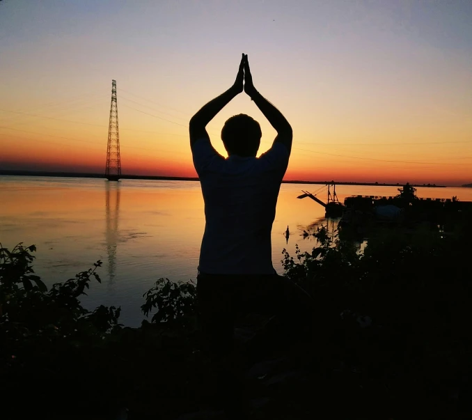 man doing yoga in front of beautiful sunset and lake