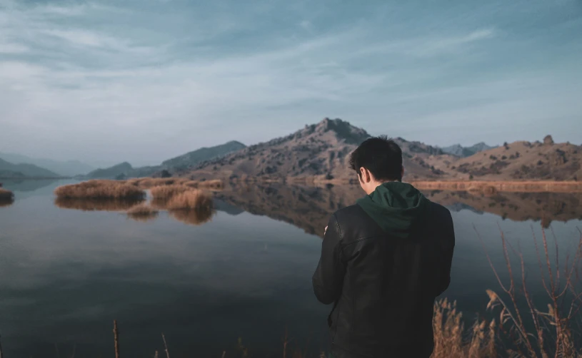 a man looking at his cell phone by a lake