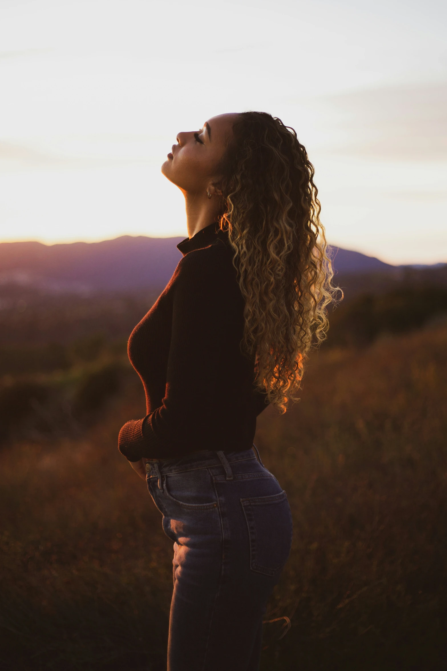 an attractive woman standing alone at sunset in a field