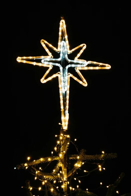 a large star ornament light up the sky on top of a tree