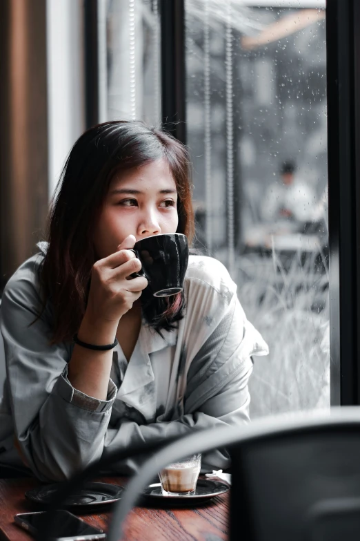 a woman holding a coffee mug while sitting in front of a window