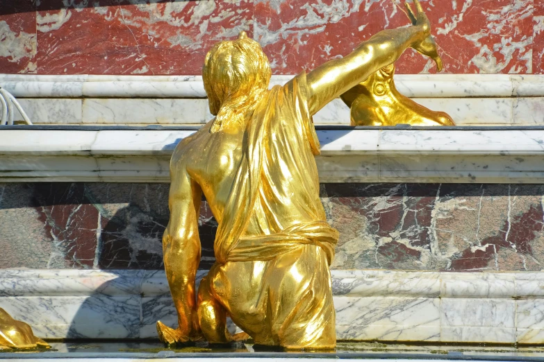 the statue is a gold color and it depicts a seated man holding a ball