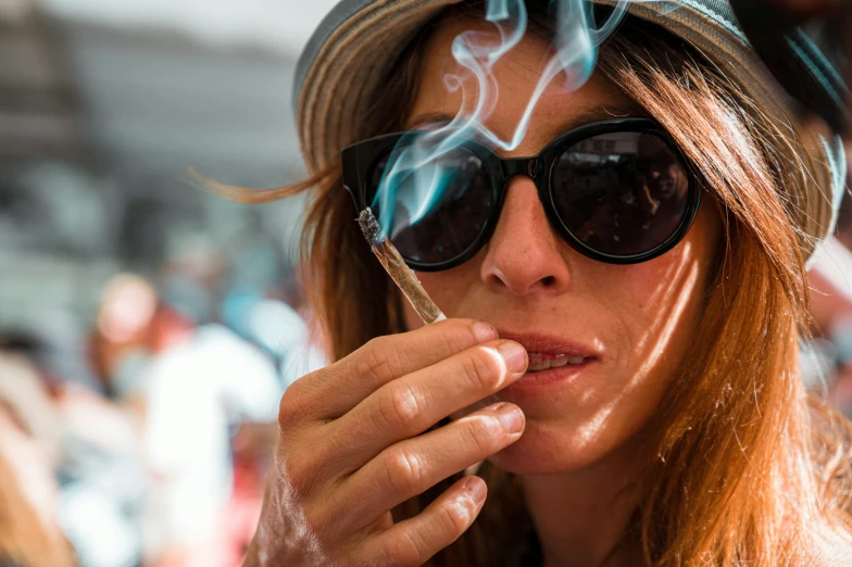 a woman in a hat and glasses lighting a cigarette