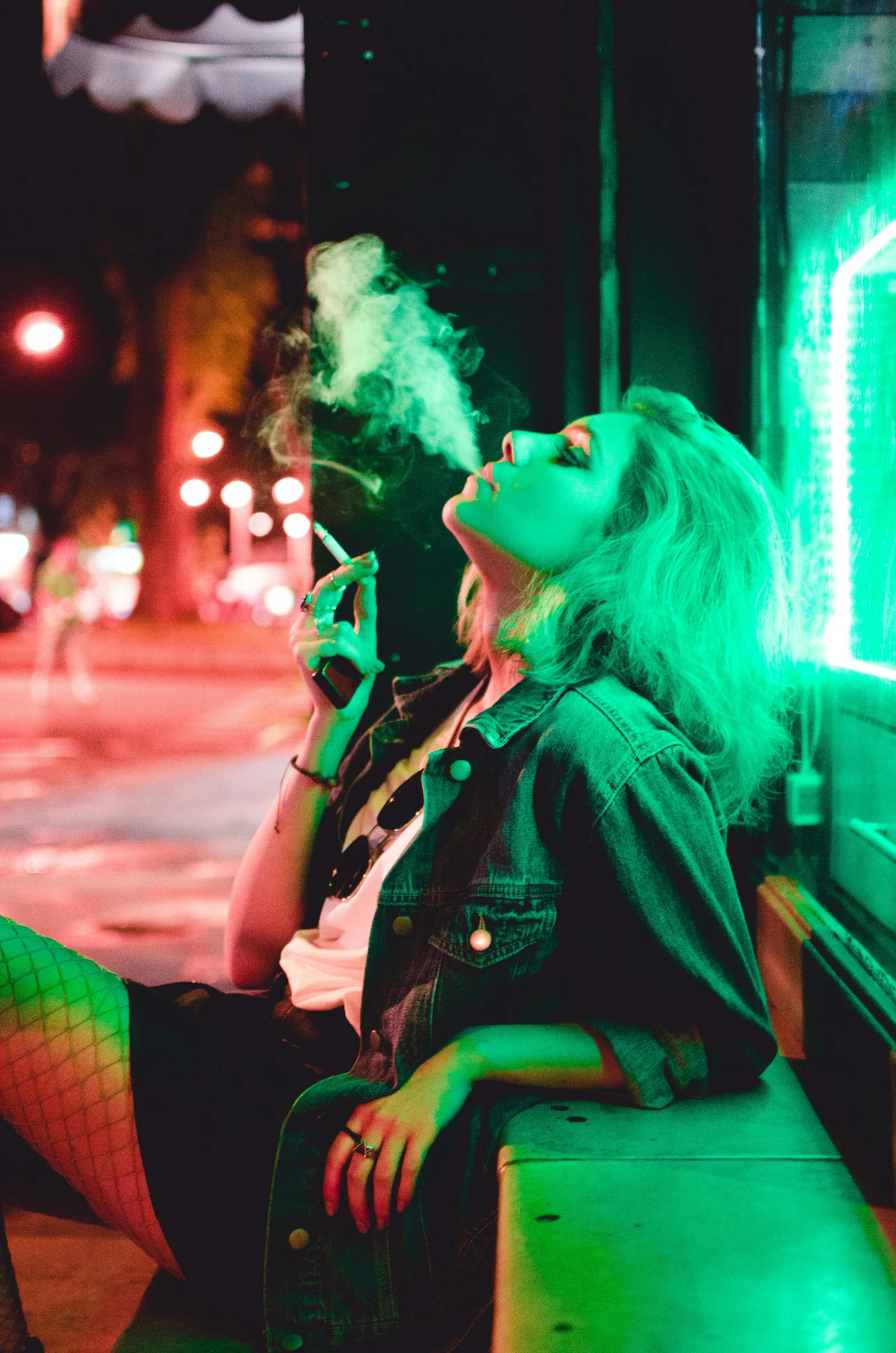 woman sitting on bench smoking with neon lights in background