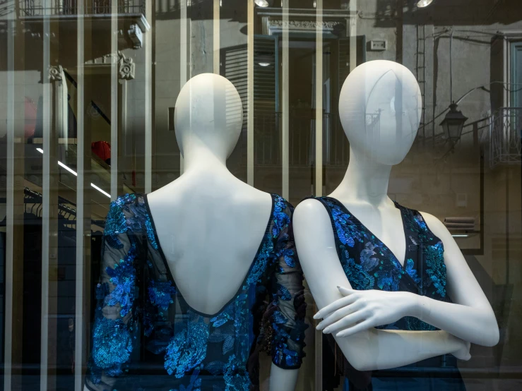 two mannequins with blue sequins in front of a window