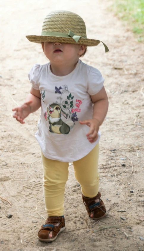 a little baby in a hat that is walking on sand
