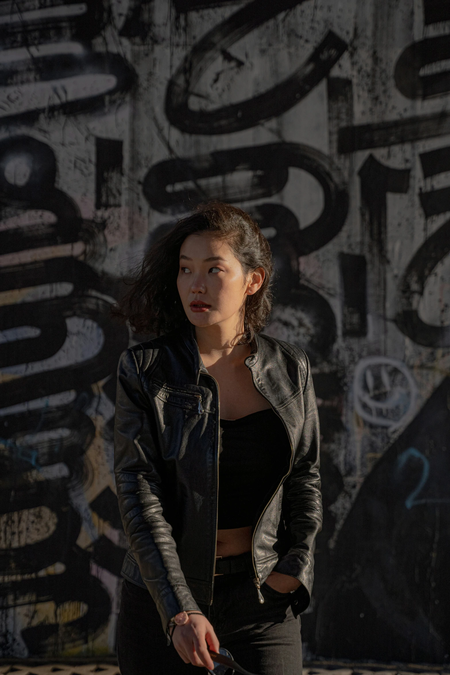 a woman standing near a wall holding a skateboard