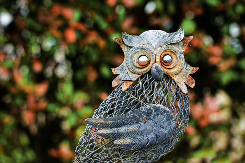 a metal owl statue with eyes wide open and a mesh netting hanging from its back