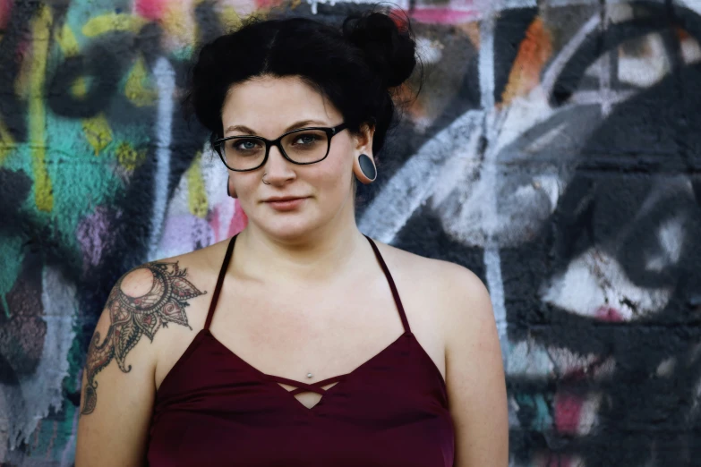 a woman with glasses standing in front of some graffiti