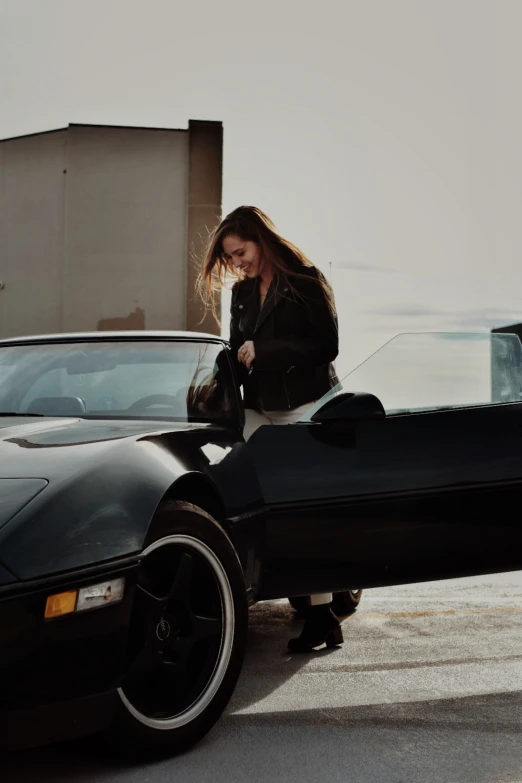 a woman is looking at the front of a black car