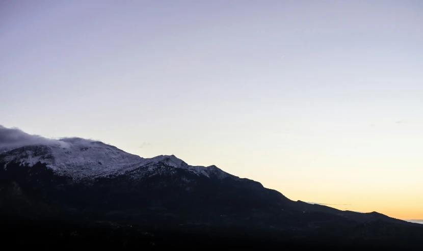 a snow capped mountain is silhouetted against a blue and orange sky