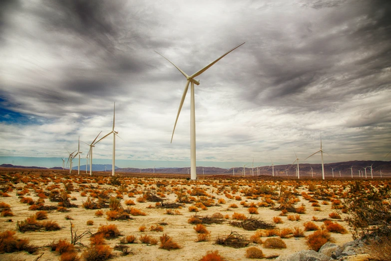 windmills are in a desert plain under a cloudy sky