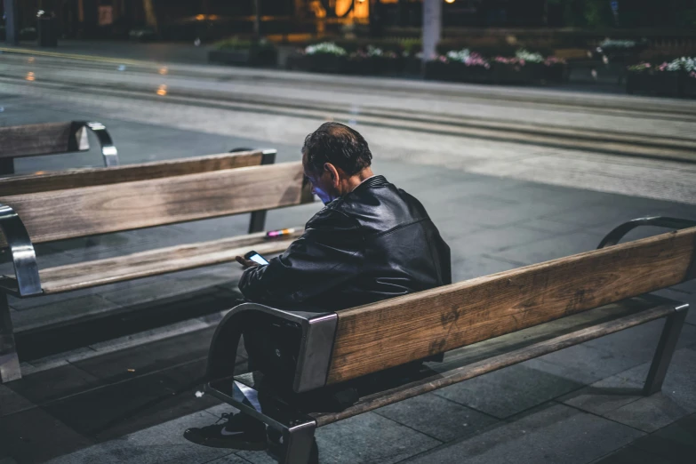 a man in leather jacket sitting on bench looking down