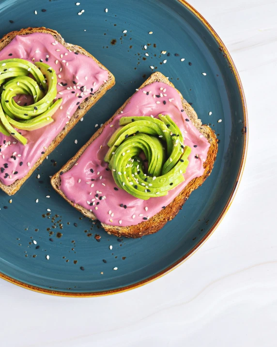 a blue plate topped with two slices of sandwich covered in pink frosting and avocado