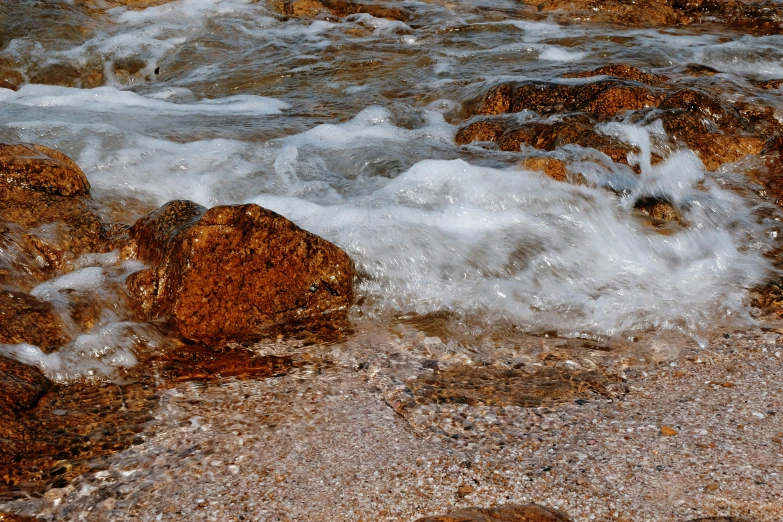 water is pouring over rocks on the beach