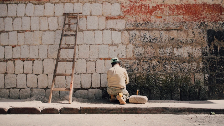 a man in beige is sitting by a brick wall