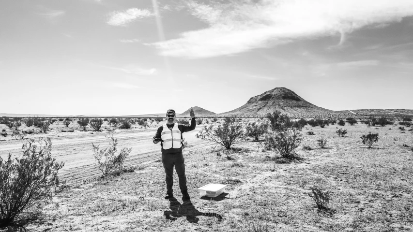 a man in desert setting holding his arms up and pointing