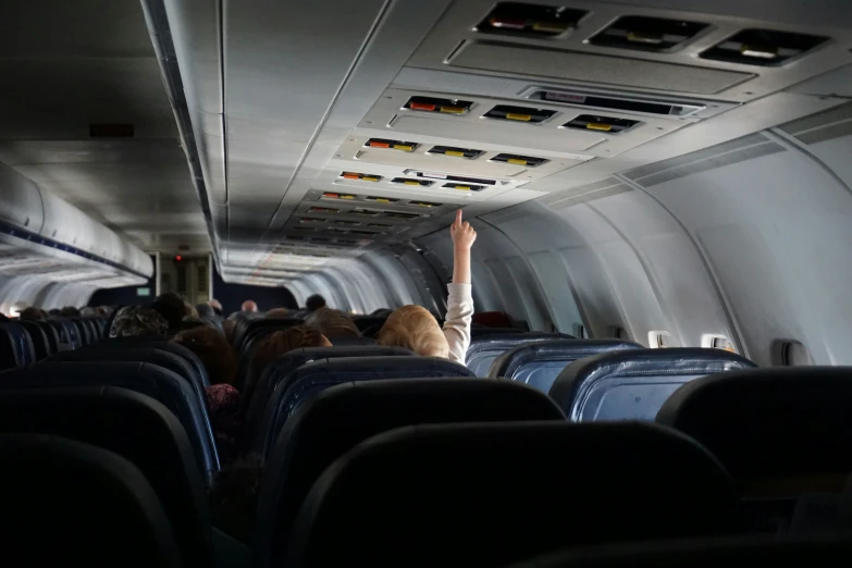 an airplane attendant raising her arm in a dimly lit airplane